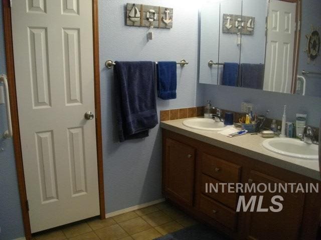 bathroom featuring a sink, baseboards, double vanity, and tile patterned flooring