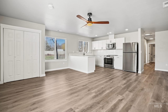 kitchen featuring white cabinetry, stainless steel appliances, kitchen peninsula, hardwood / wood-style flooring, and tasteful backsplash