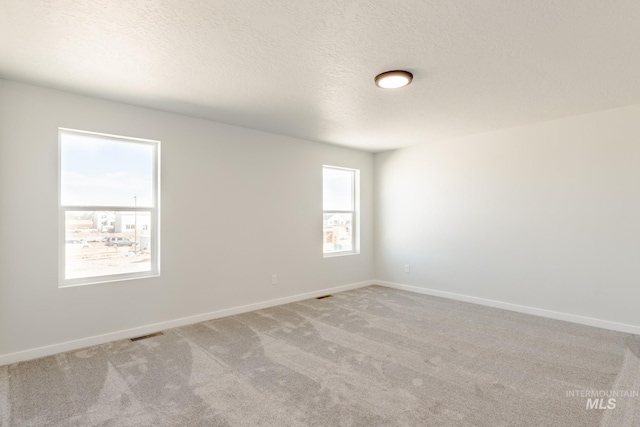 spare room featuring visible vents, baseboards, light colored carpet, and a textured ceiling