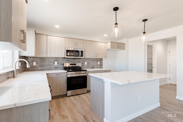 kitchen featuring a sink, light wood-type flooring, light stone counters, and appliances with stainless steel finishes