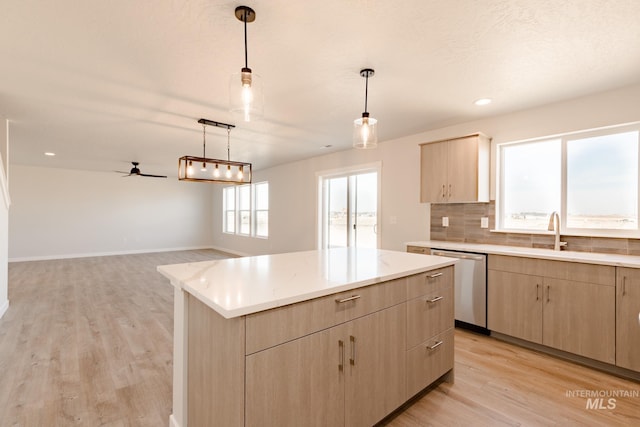 kitchen featuring stainless steel dishwasher, decorative backsplash, a sink, and light brown cabinetry