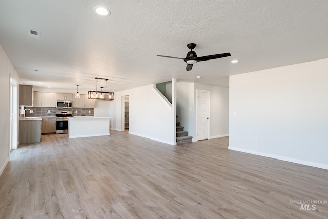 unfurnished living room with baseboards, stairway, light wood-style flooring, a ceiling fan, and a sink