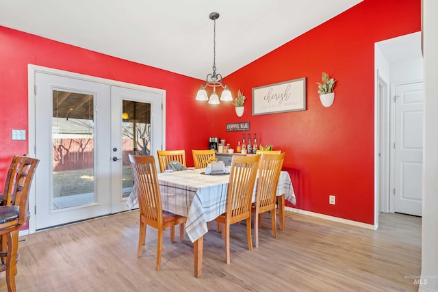 dining area with light wood-style flooring, an accent wall, baseboards, vaulted ceiling, and french doors