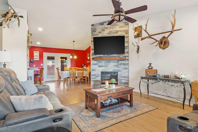 living area featuring french doors, a fireplace, lofted ceiling, a ceiling fan, and wood finished floors