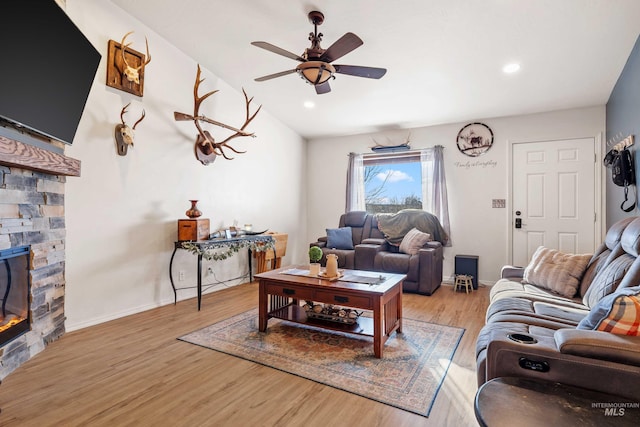 living room with recessed lighting, light wood-style flooring, ceiling fan, a stone fireplace, and baseboards