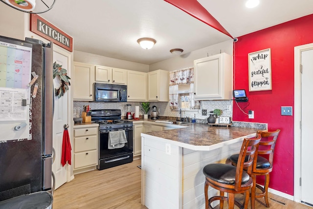 kitchen with a sink, backsplash, black appliances, light wood finished floors, and a kitchen bar