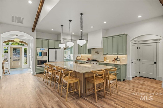 25580 Gooseberry Ln, Caldwell, ID 83607 - kitchen with green cabinets, custom exhaust hood, light wood-style flooring, stainless steel double oven, and a breakfast bar area