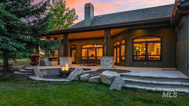 25580 Gooseberry Ln, Caldwell, ID 83607 - back of house at dusk featuring a fire pit, a chimney, a shingled roof, and board and batten siding