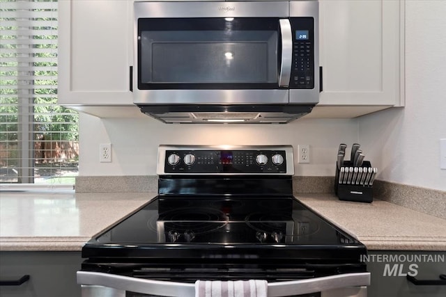 kitchen with white cabinets, electric range, stainless steel microwave, and light countertops