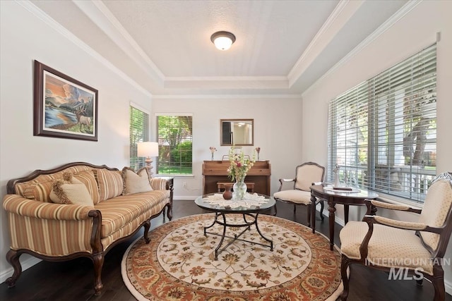 living area featuring baseboards, a tray ceiling, crown molding, and wood finished floors