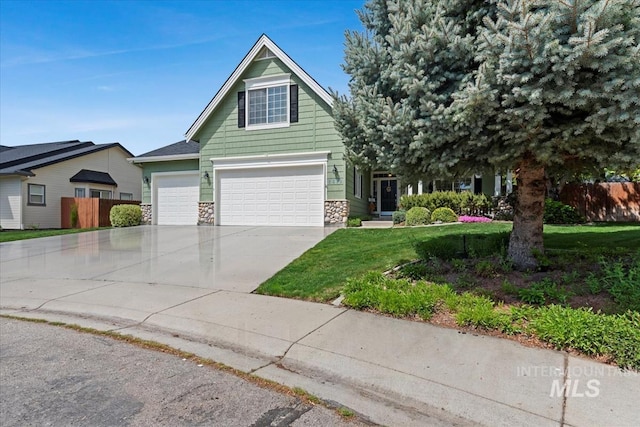 view of front of property featuring a garage, fence, stone siding, a front yard, and driveway
