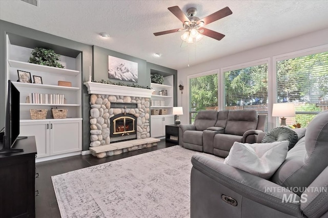 living area featuring a stone fireplace, a ceiling fan, a textured ceiling, and dark wood-type flooring