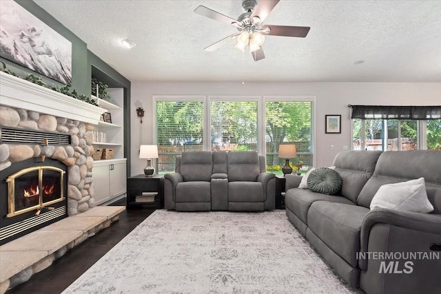 living area with a stone fireplace, a ceiling fan, a textured ceiling, and wood finished floors