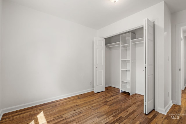 unfurnished bedroom with baseboards, wood finished floors, and a closet
