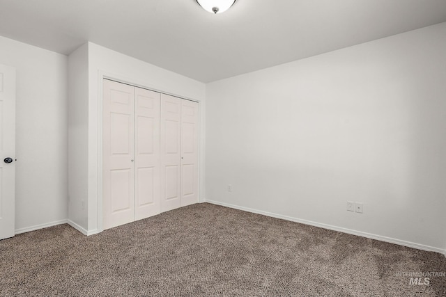 unfurnished bedroom with baseboards, a closet, and dark colored carpet