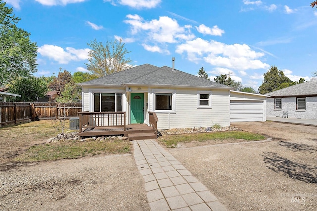 bungalow-style house featuring central air condition unit, fence, a shingled roof, and a detached garage