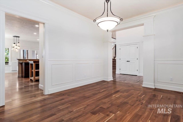 unfurnished dining area featuring wainscoting, a notable chandelier, dark wood-style floors, and a decorative wall