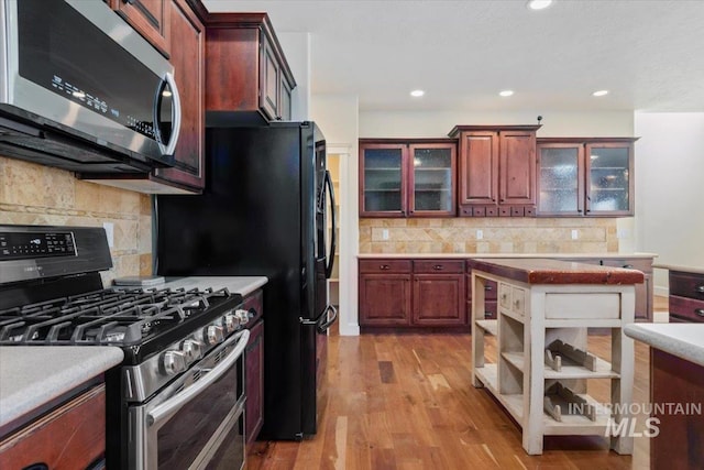 kitchen featuring glass insert cabinets, appliances with stainless steel finishes, tasteful backsplash, light countertops, and light wood-style floors