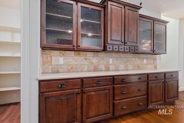 kitchen featuring light countertops, dark wood-style flooring, glass insert cabinets, and tasteful backsplash