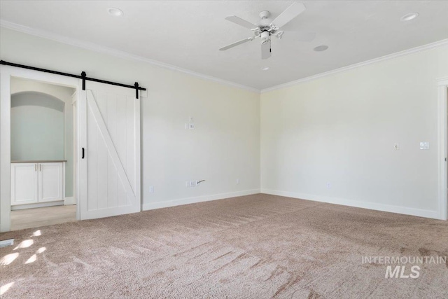 empty room with crown molding, a ceiling fan, baseboards, a barn door, and carpet flooring