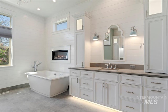 bathroom with a freestanding tub, vanity, a glass covered fireplace, and visible vents