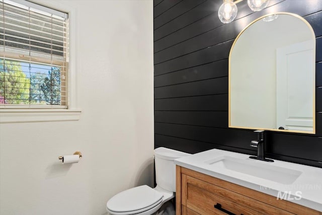 bathroom with wooden walls, vanity, and toilet