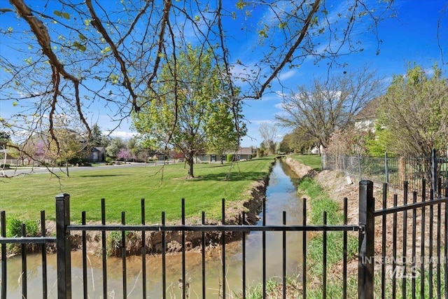 view of home's community featuring fence, a water view, and a lawn