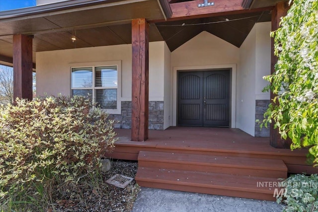 property entrance with a porch, stucco siding, and stone siding