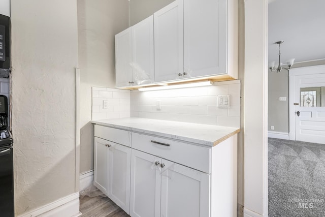 kitchen featuring light carpet, light stone countertops, tasteful backsplash, a notable chandelier, and white cabinetry