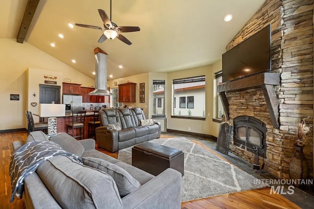 living room with ceiling fan, high vaulted ceiling, beamed ceiling, hardwood / wood-style floors, and a stone fireplace