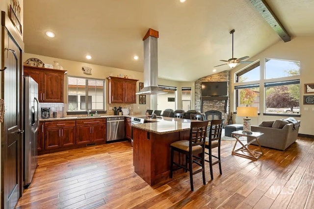 kitchen with a breakfast bar area, decorative backsplash, a fireplace, appliances with stainless steel finishes, and island exhaust hood