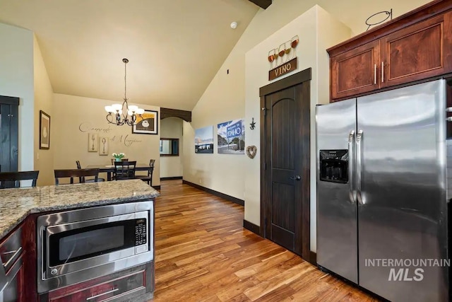 kitchen with light stone countertops, appliances with stainless steel finishes, vaulted ceiling, and a notable chandelier