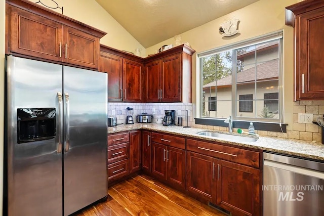 kitchen with backsplash, sink, vaulted ceiling, appliances with stainless steel finishes, and light stone counters