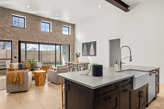 kitchen featuring brick wall, a sink, dark brown cabinetry, a towering ceiling, and light wood-type flooring