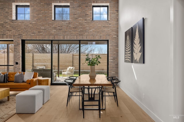 dining room featuring brick wall, baseboards, a high ceiling, and light wood-style floors