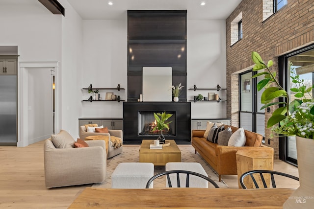 living area with a warm lit fireplace, brick wall, a high ceiling, and wood finished floors