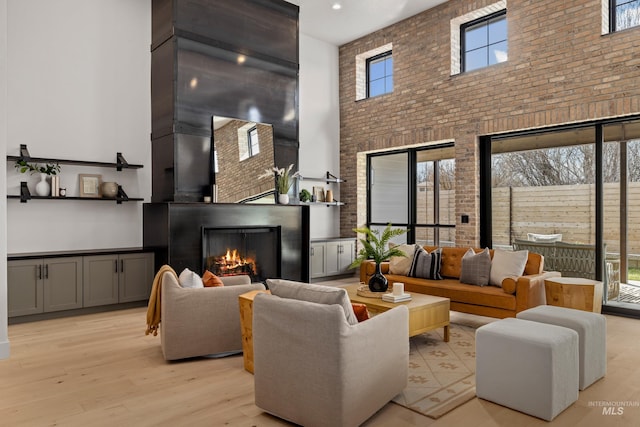 living area with brick wall, light wood finished floors, a towering ceiling, and a lit fireplace