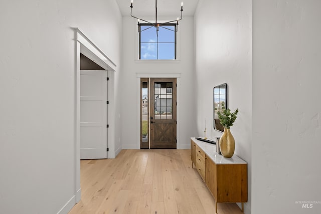 entryway featuring light wood-style flooring, baseboards, and a towering ceiling