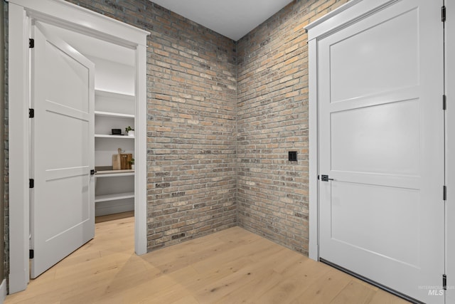 empty room featuring brick wall and light wood finished floors