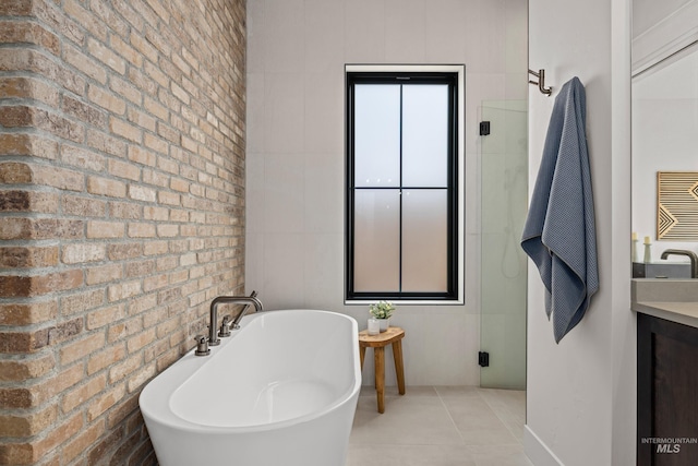 full bath featuring tile patterned floors, a freestanding bath, brick wall, and vanity