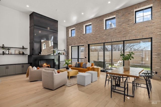 living room featuring a glass covered fireplace, a high ceiling, light wood-style floors, and a healthy amount of sunlight