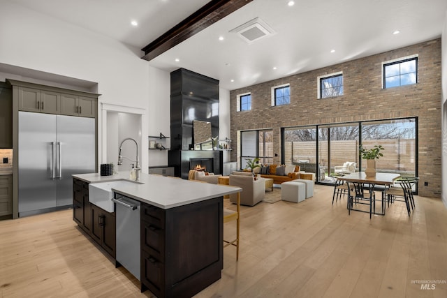 kitchen featuring a large fireplace, a high ceiling, appliances with stainless steel finishes, and light wood finished floors