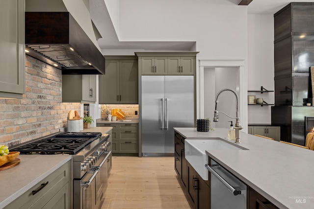 kitchen featuring high quality appliances, a sink, wall chimney range hood, light wood finished floors, and light countertops