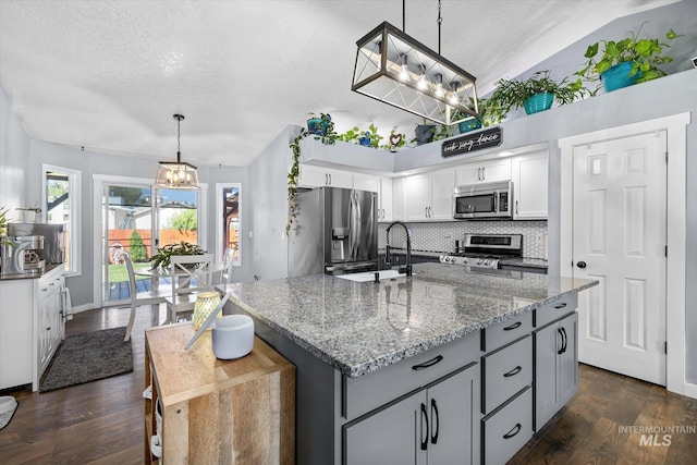 kitchen with backsplash, dark wood-style flooring, a sink, a chandelier, and stainless steel appliances