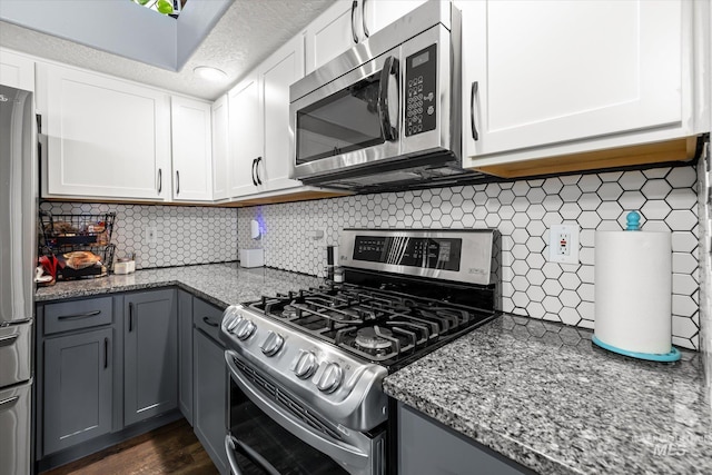 kitchen with appliances with stainless steel finishes, gray cabinets, light stone countertops, and backsplash