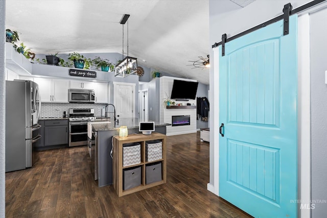 kitchen featuring a glass covered fireplace, lofted ceiling, open floor plan, a barn door, and stainless steel appliances