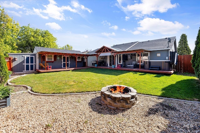 back of property featuring a lawn, a deck, fence, and a fire pit