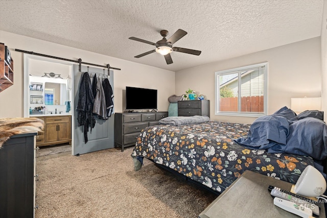 bedroom featuring a textured ceiling, a barn door, light carpet, and ensuite bath
