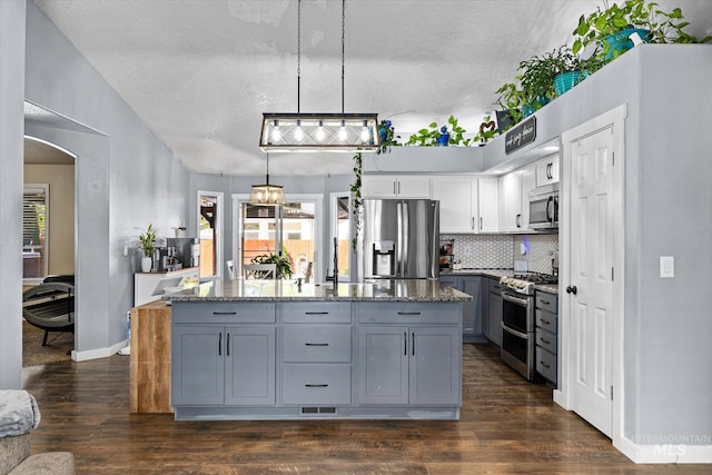 kitchen featuring gray cabinets, a kitchen island, backsplash, arched walkways, and stainless steel appliances