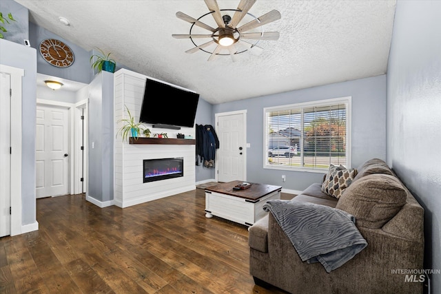 living room featuring a ceiling fan, a textured ceiling, wood finished floors, baseboards, and a glass covered fireplace